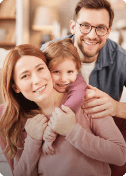 A family portrait featuring a man, a woman, and a child, all smiling together in a warm, outdoor setting.