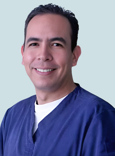 Dr. Carlos Argote, dentist, poses in his clinic, showcasing a welcoming smile.