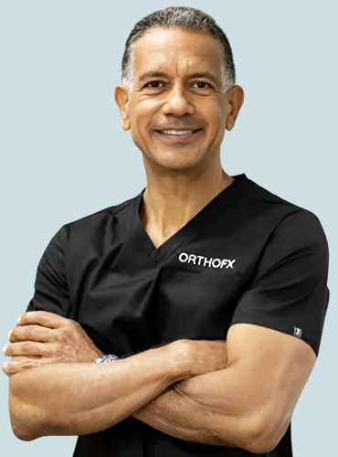 Dr. Efrain Chara in scrubs stands with his arms crossed, exuding confidence and professionalism.