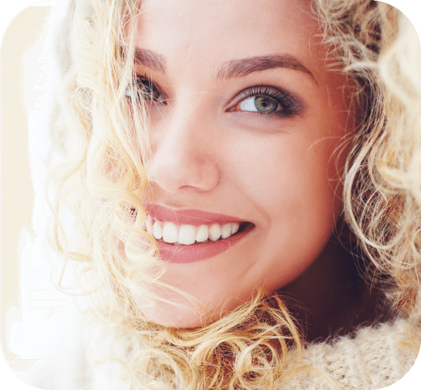 A woman with curly hair wearing a white sweater, smiling softly against a neutral background.