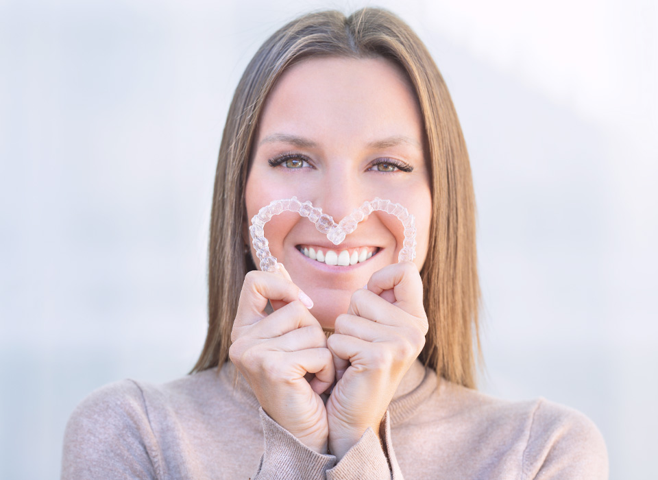 A woman holds a heart-shaped plastic device, smiling as she showcases it in her hands.